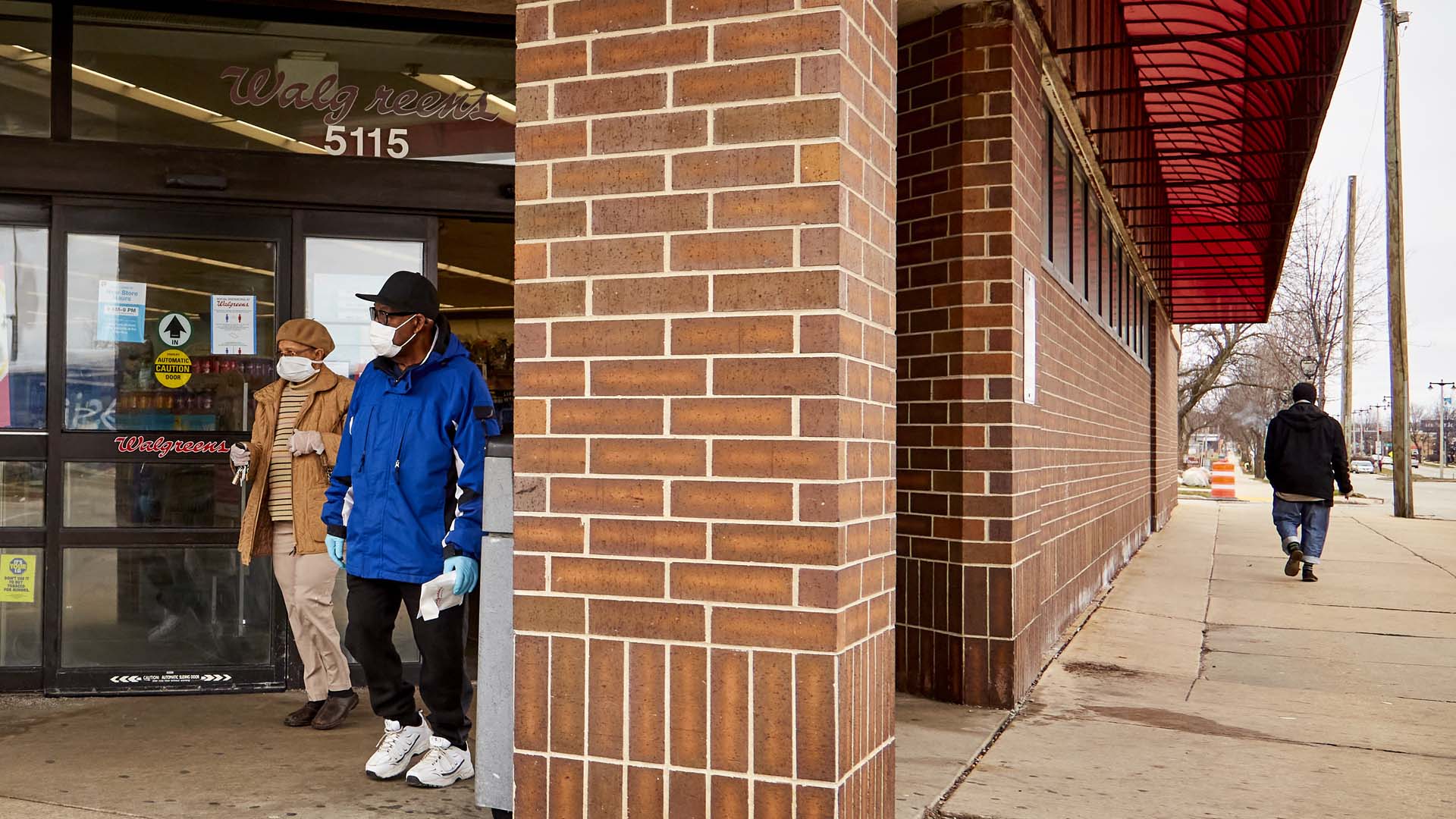 A couple wearing face coverings and wearing rubber gloves leave a Walgreens in Milwaukee, Wisconsin.