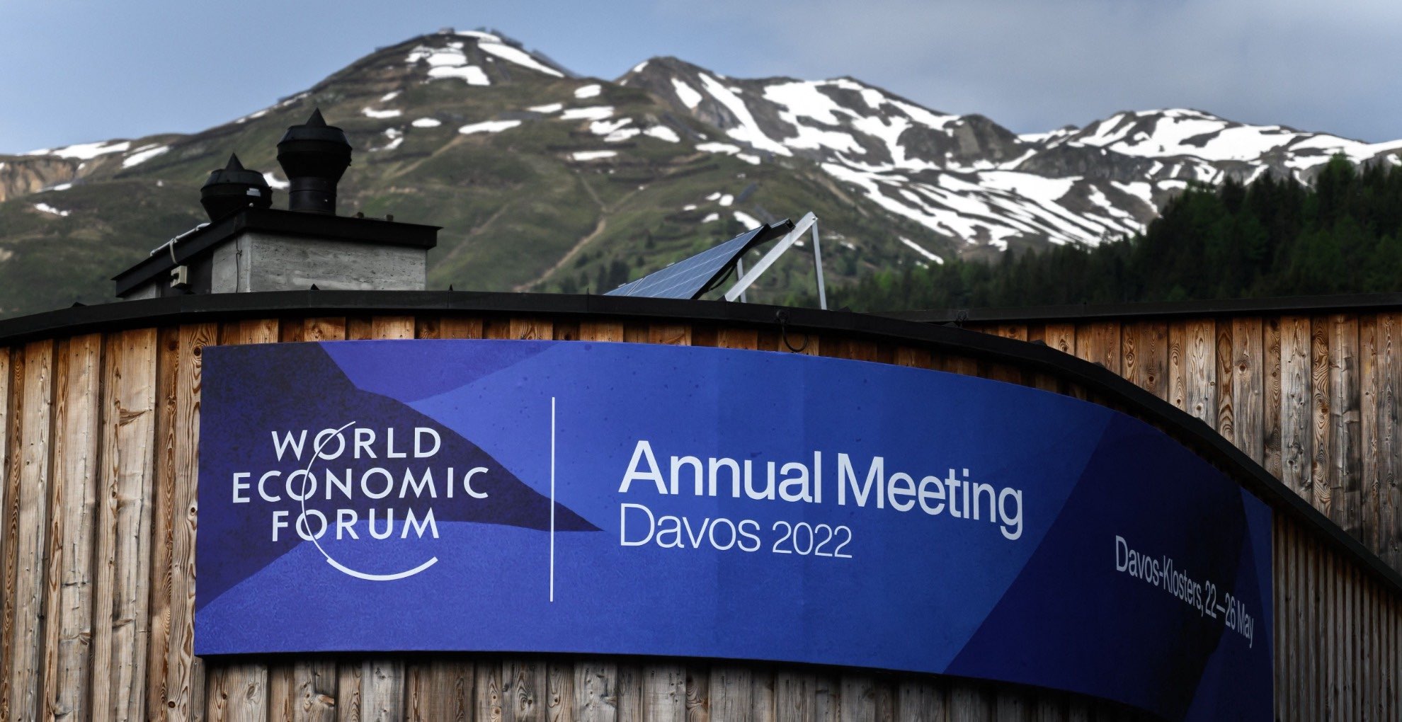 A banner on the congress centre in Davos with a banner. Mountains appear in the background,=,