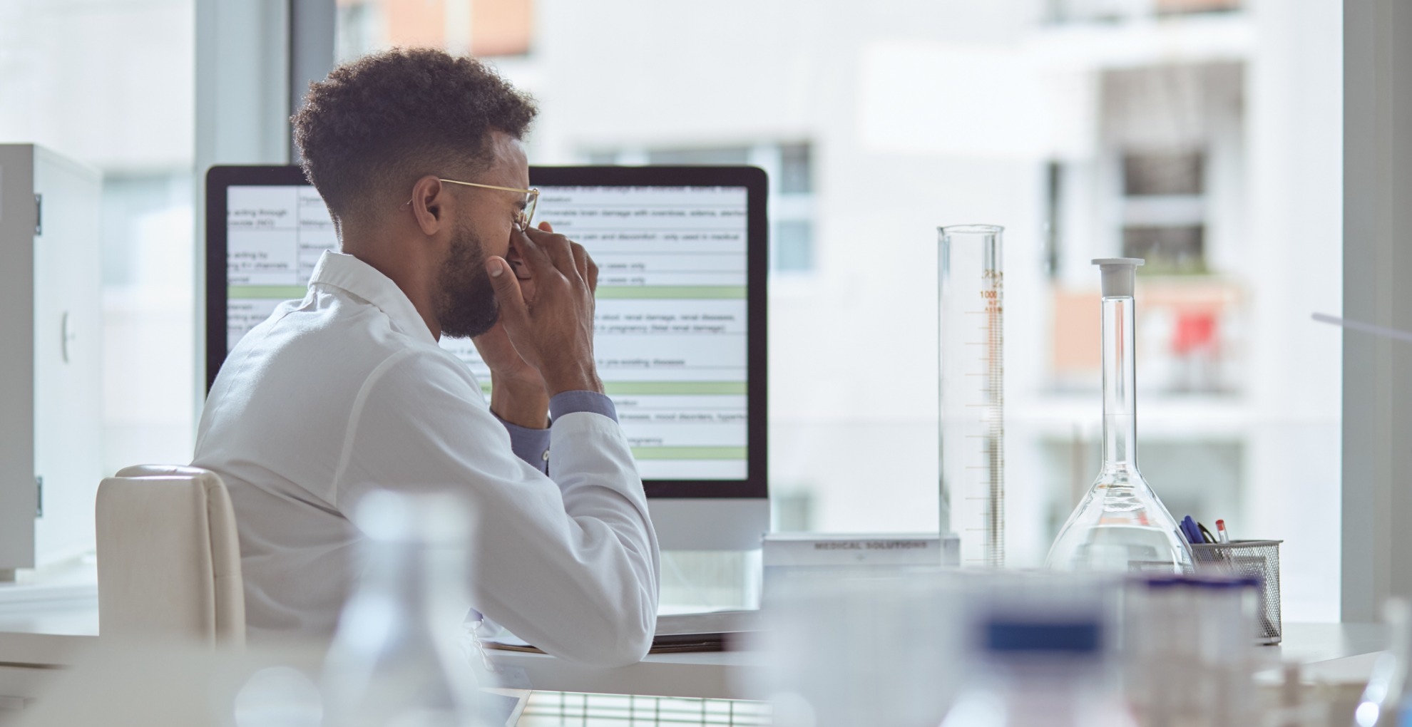 A scientist appears stressed in their lab while working on a draft on their computer